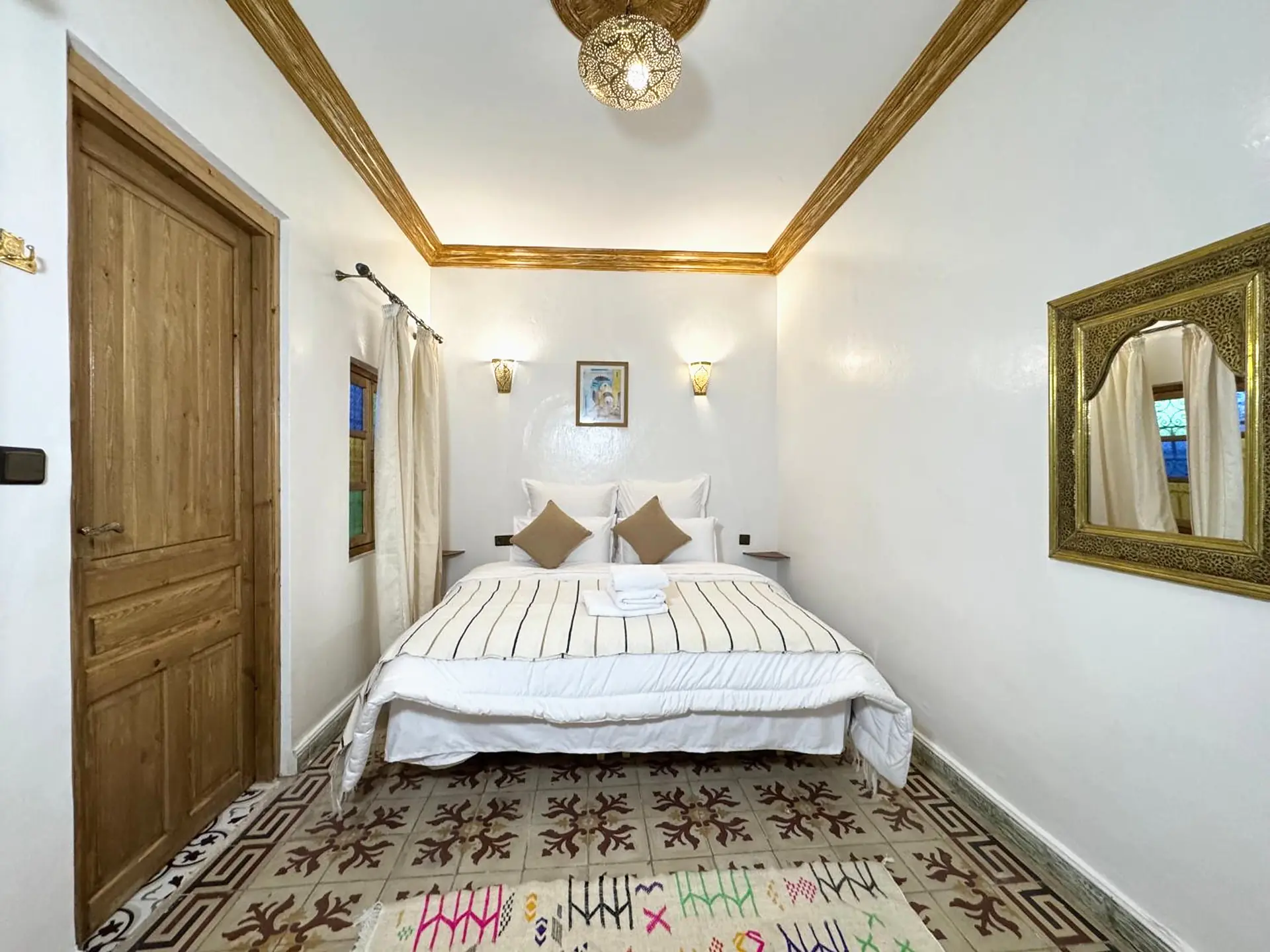 La chambre double climatisée, son lit blanc et son miroir doré